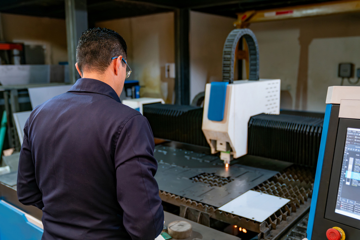 Latin American engineer watching a laser machine cutting a metal sheet at a factory - manufacturing concepts