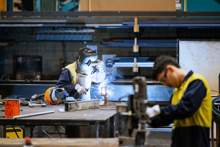 Large industrial warehouse with machinery and yellow support structures , with steel and metal processing equipment, welders welding steel bars
