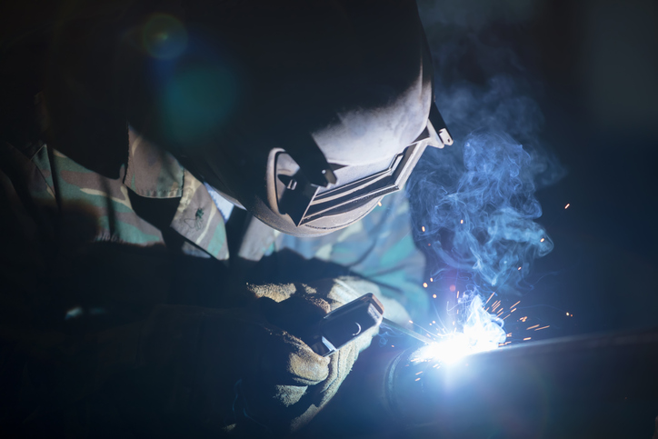 Welder at work. Man in a protective mask. The welder makes seams on the metal. Sparks and smoke when welding.