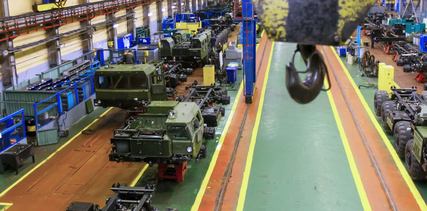 Workers assemble military vehicles in a spacious factory with various machinery and tools present, showcasing an industrial environment.