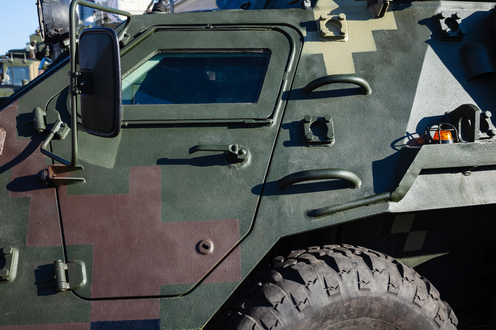 Wheels and front part of the armored personnel carrier. Camouflage green color of military vehicles. Side view. Khaki background.